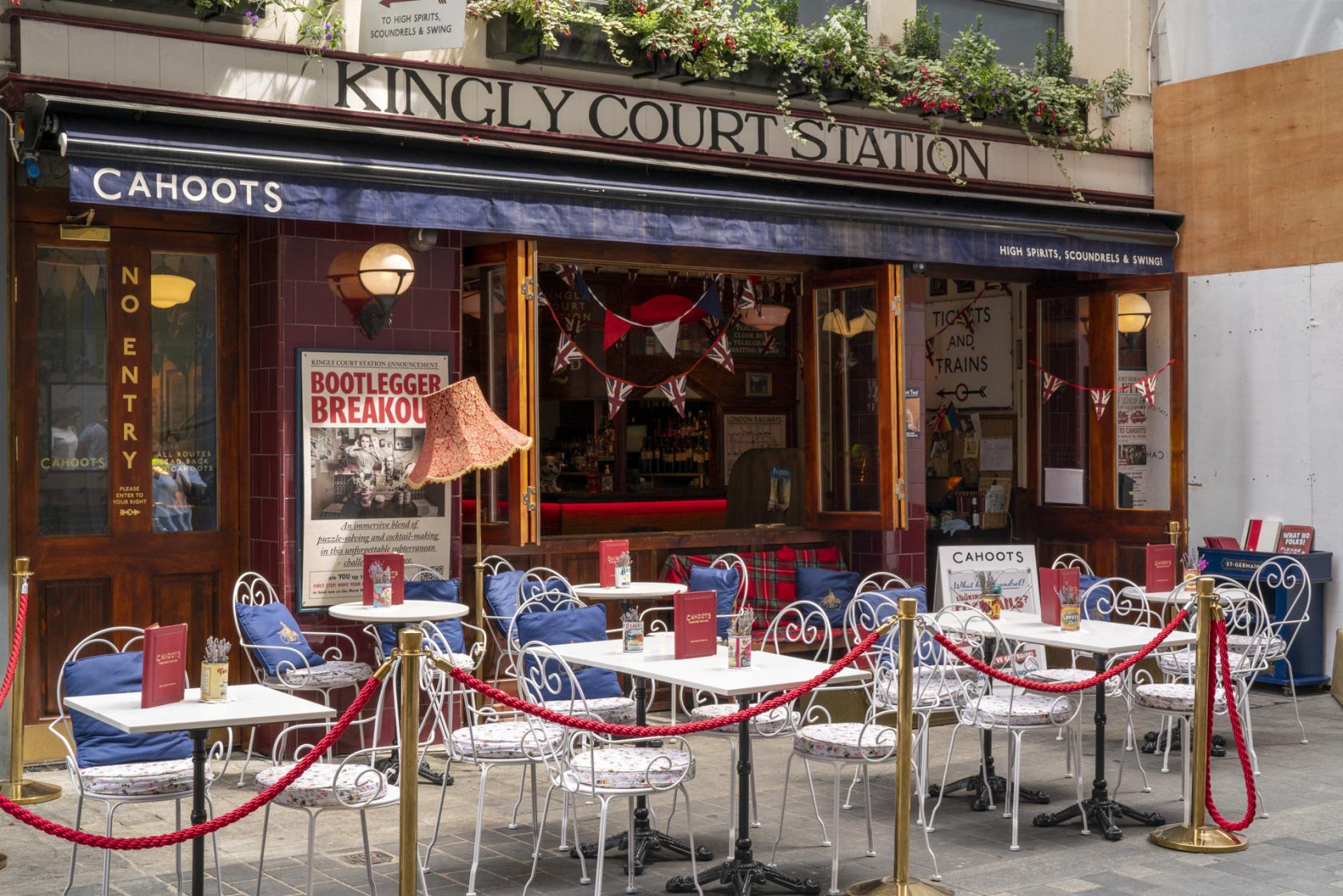 An outdoor pub area with white metal tables, red menus, and a café-style setup at Cahoots.