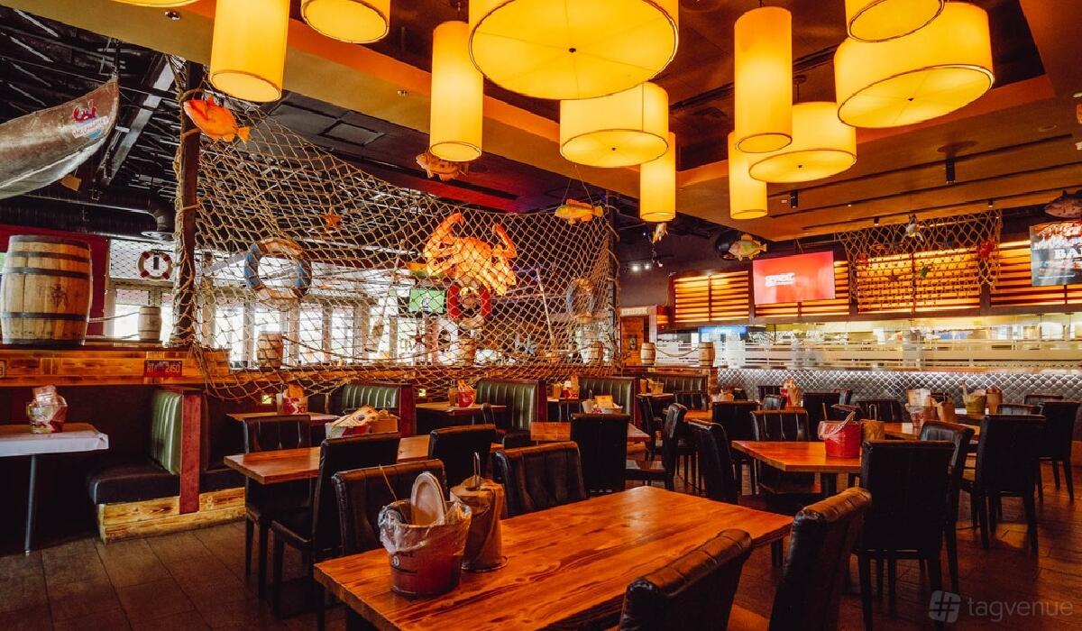 A restaurant with wooden tables, booth seating, hanging lantern lights, and fishing net decor at Mr.Crabby's Cajun Seafood & Bar.