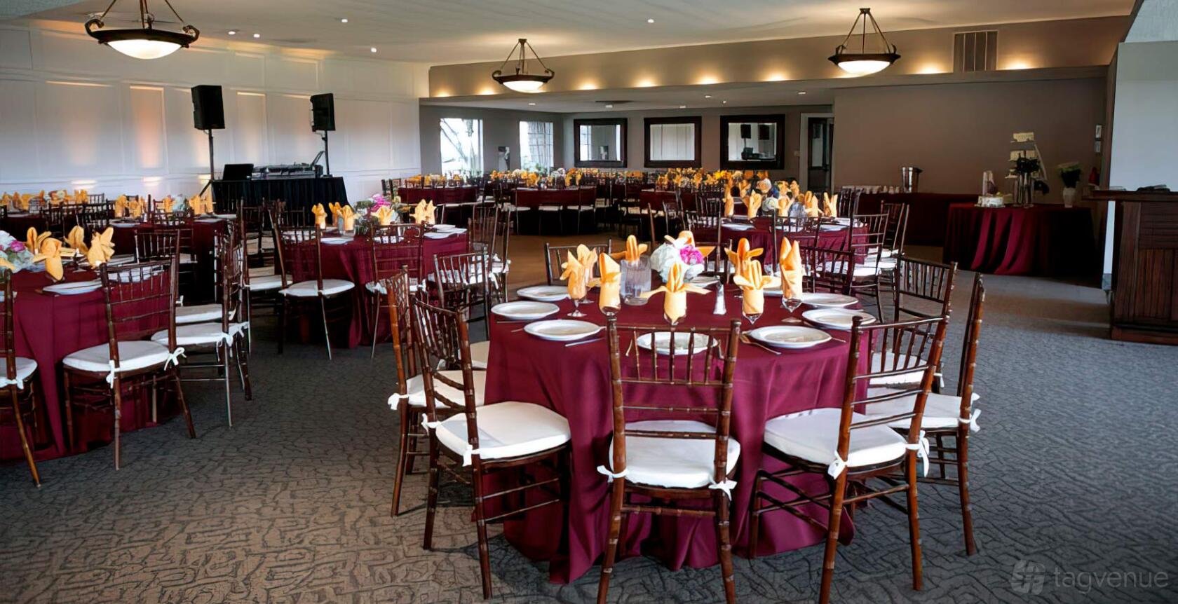 An indoor event venue with round tables dressed in burgundy linens, banquet chairs, and folded napkins at Tustin Hills Racquet Club - Legacy Ballroom.