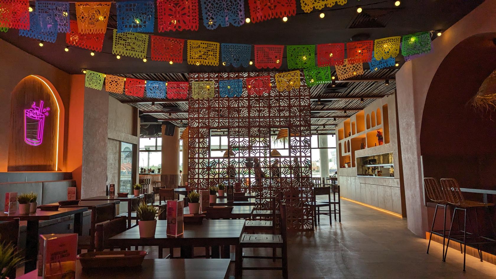 A restaurant with colorful papel picado banners, wooden tables, and decorative lattice dividers at Chimichanga Vivocity.