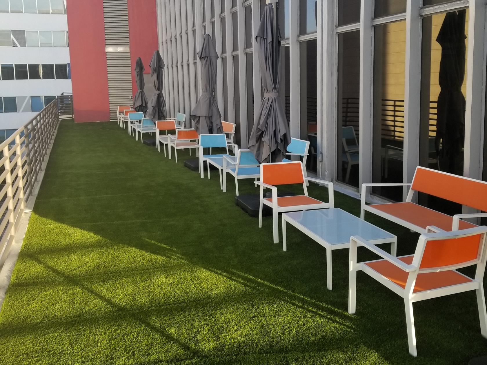 An outdoor meeting terrace with artificial grass, colorful lounge chairs, and closed umbrellas at Momentum Business Center.