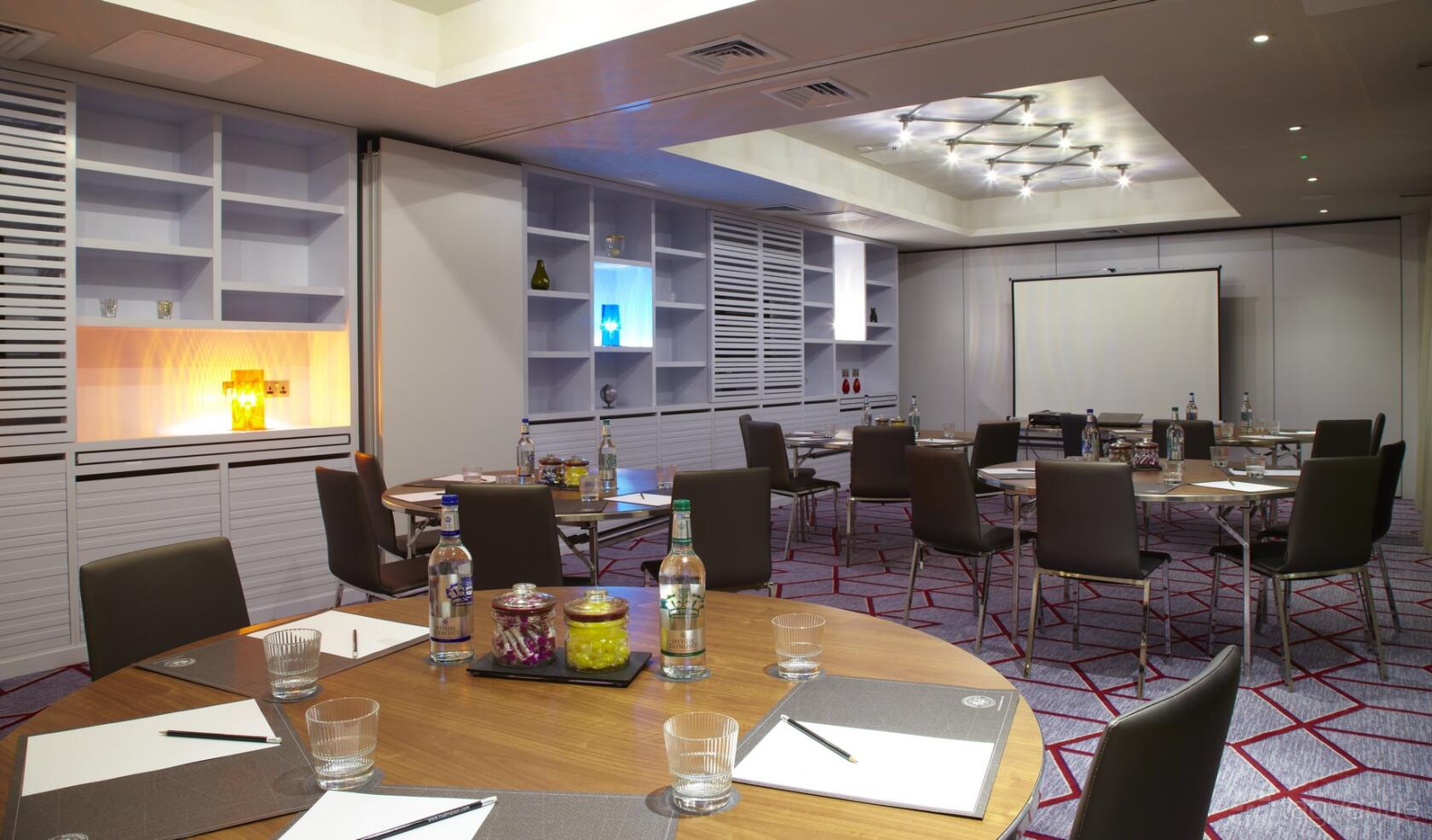 A meeting room with round tables, bottled water, notepads, and built-in shelving at Malmaison Glasgow.