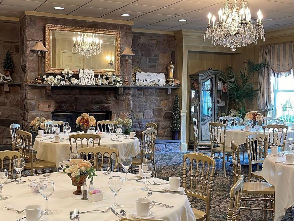 A function room with round tables, gold chairs, floral centerpieces, chandeliers, and a stone fireplace at The Buck Hotel.