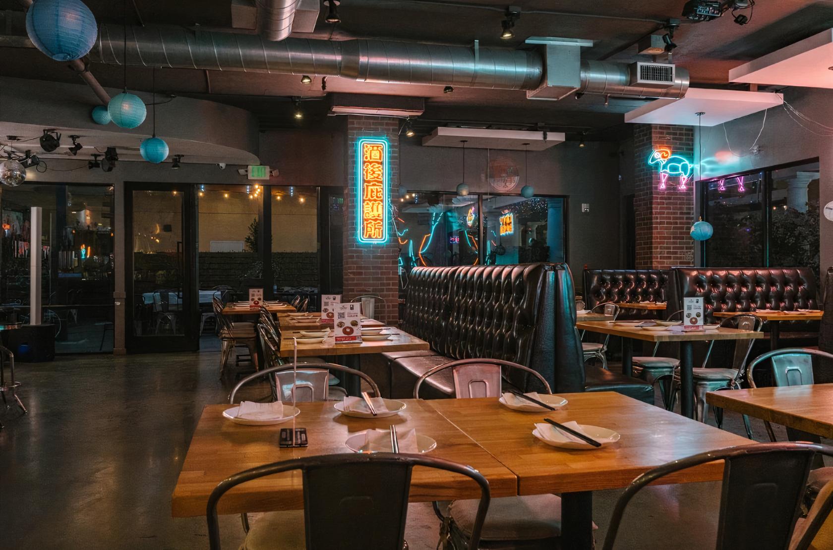 A restaurant with tufted leather booths, exposed brick walls, neon signs, and wooden tables at Tang Dynasty.