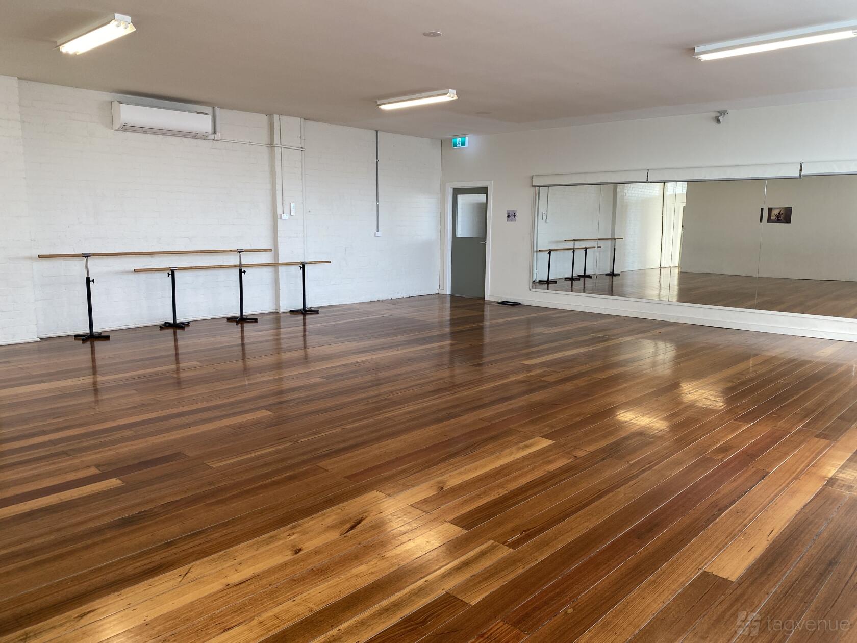 A rehearsal room with polished wooden floors, wall-mounted ballet barres, and a large wall mirror at Rain & Lucky Academy of Dance.