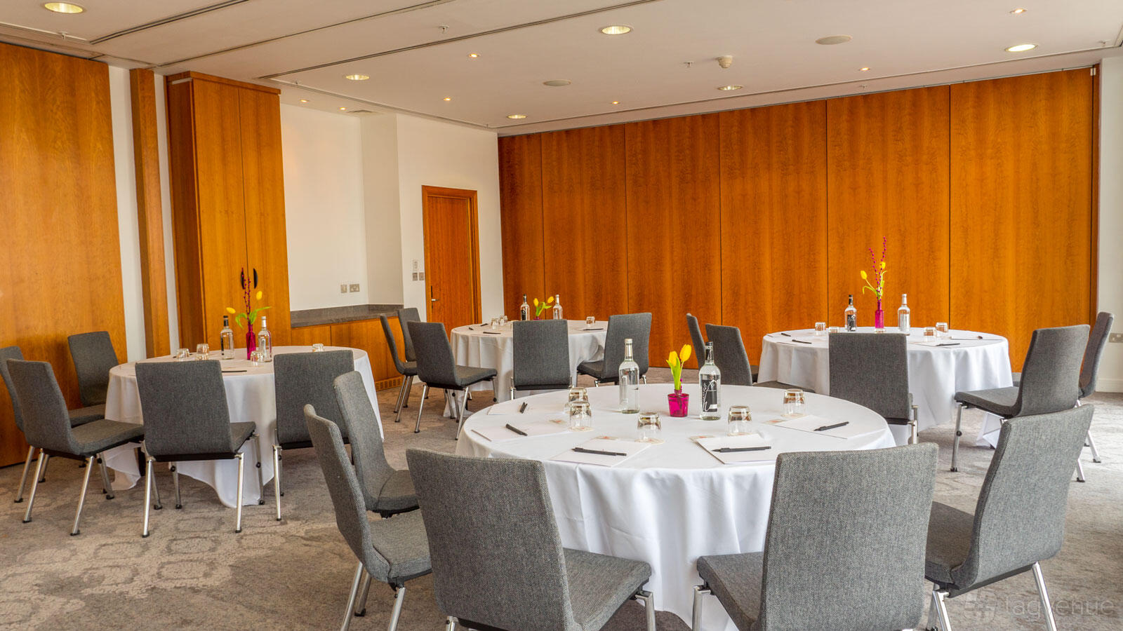 A hotel meeting room with round tables, grey chairs, and wood-paneled walls at The Lowry Hotel.