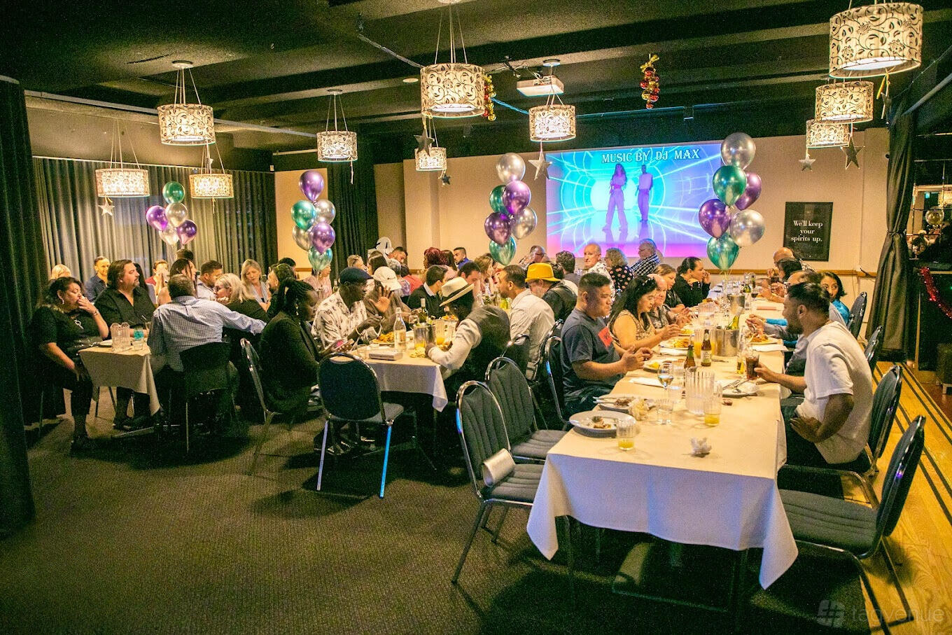 A restaurant event space with banquet tables, patterned pendant lights, and a projection screen at River Canyon Venue & Function Centre.