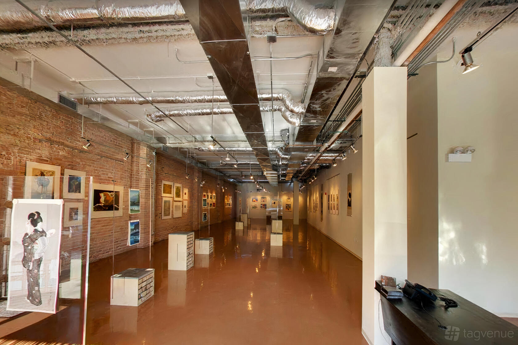 A gallery with exposed brick walls, industrial ceilings, and framed artwork displayed at Floating World Gallery.