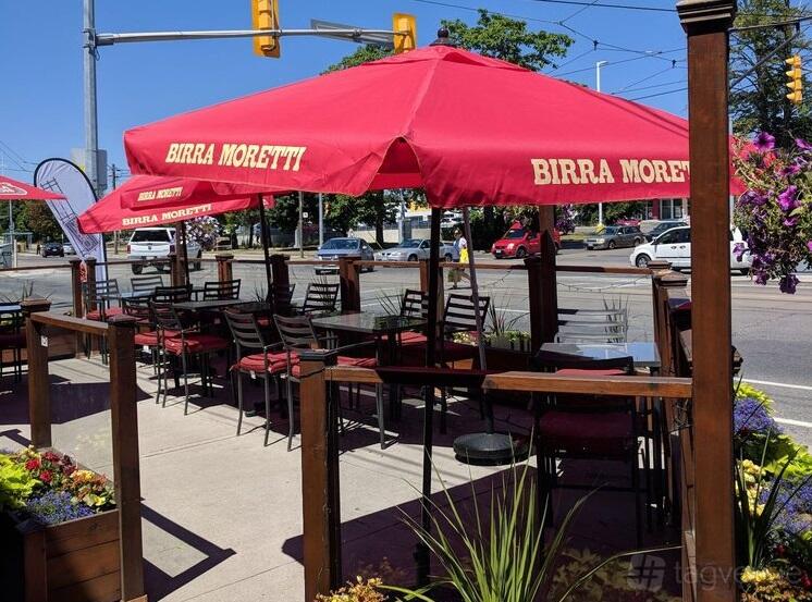 A restaurant terrace with red Birra Moretti umbrellas, wooden tables, and planters along the railing at Pulcinella.