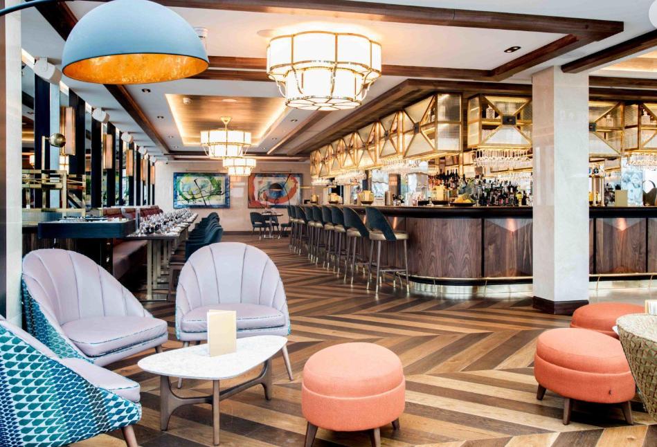 A rooftop bar with herringbone wood floors, plush lounge seating, and a curved bar at Aviary Rooftop Bar & Restaurant.