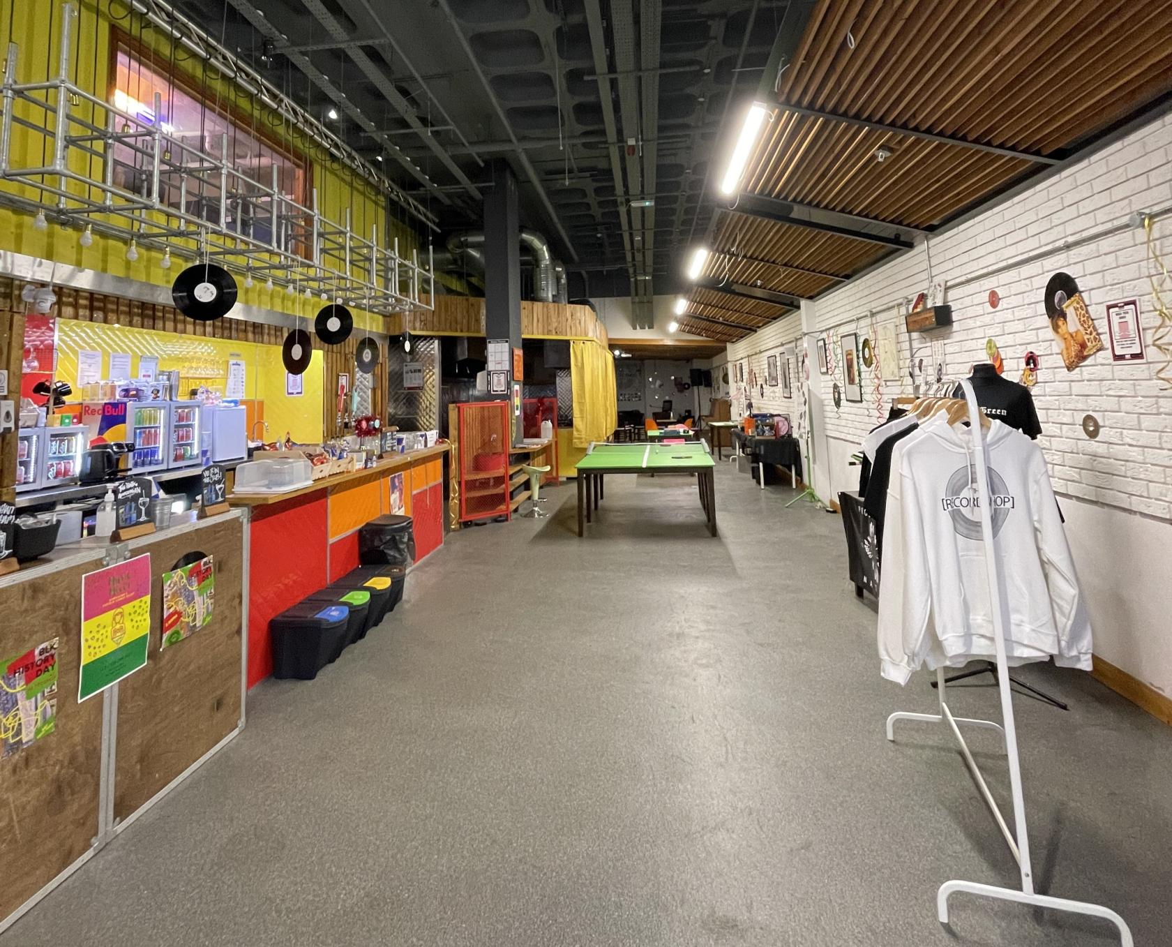 An event space with a pool table, record decorations, a refreshment counter, and merchandise rack at The RecordShop.