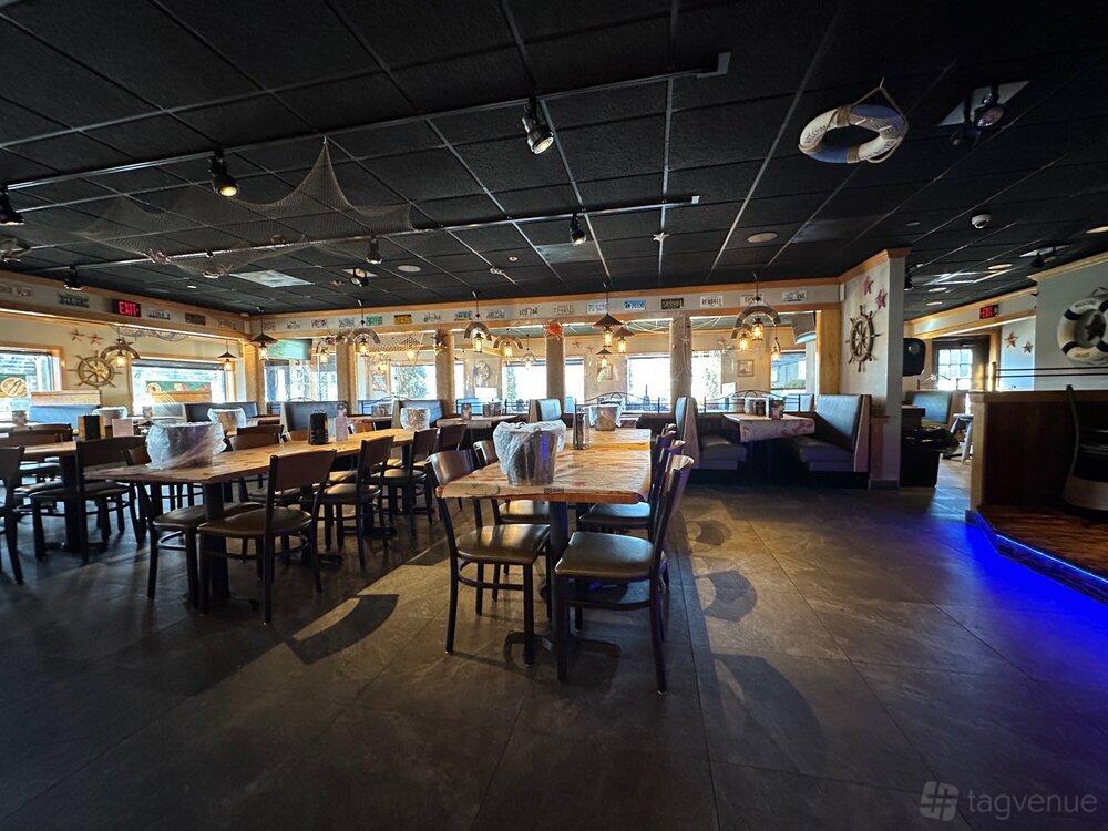A restaurant with wooden tables, cushioned booths, nautical decor, and large windows at Hook & Reel- Union.