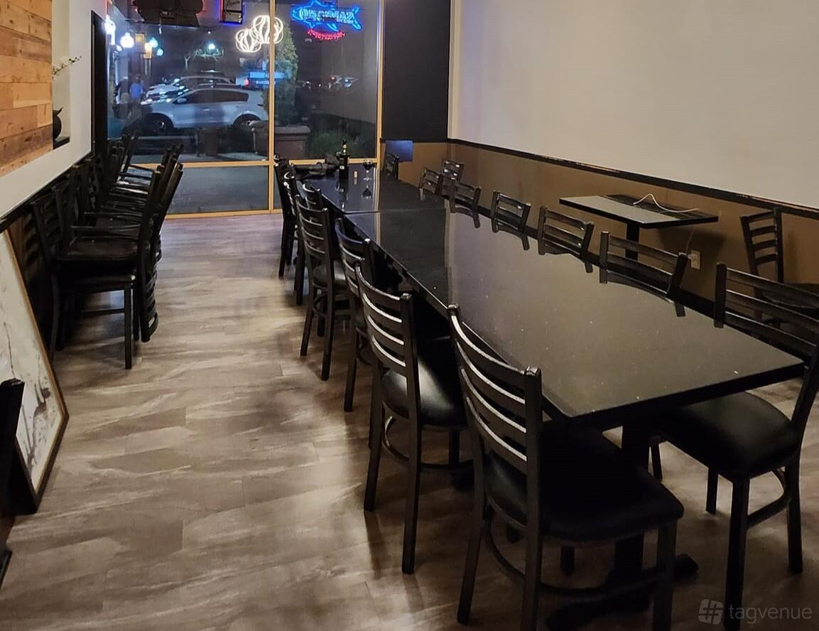 A dining room with a long black table, black chairs, and wood accents at Taiko Sushi.