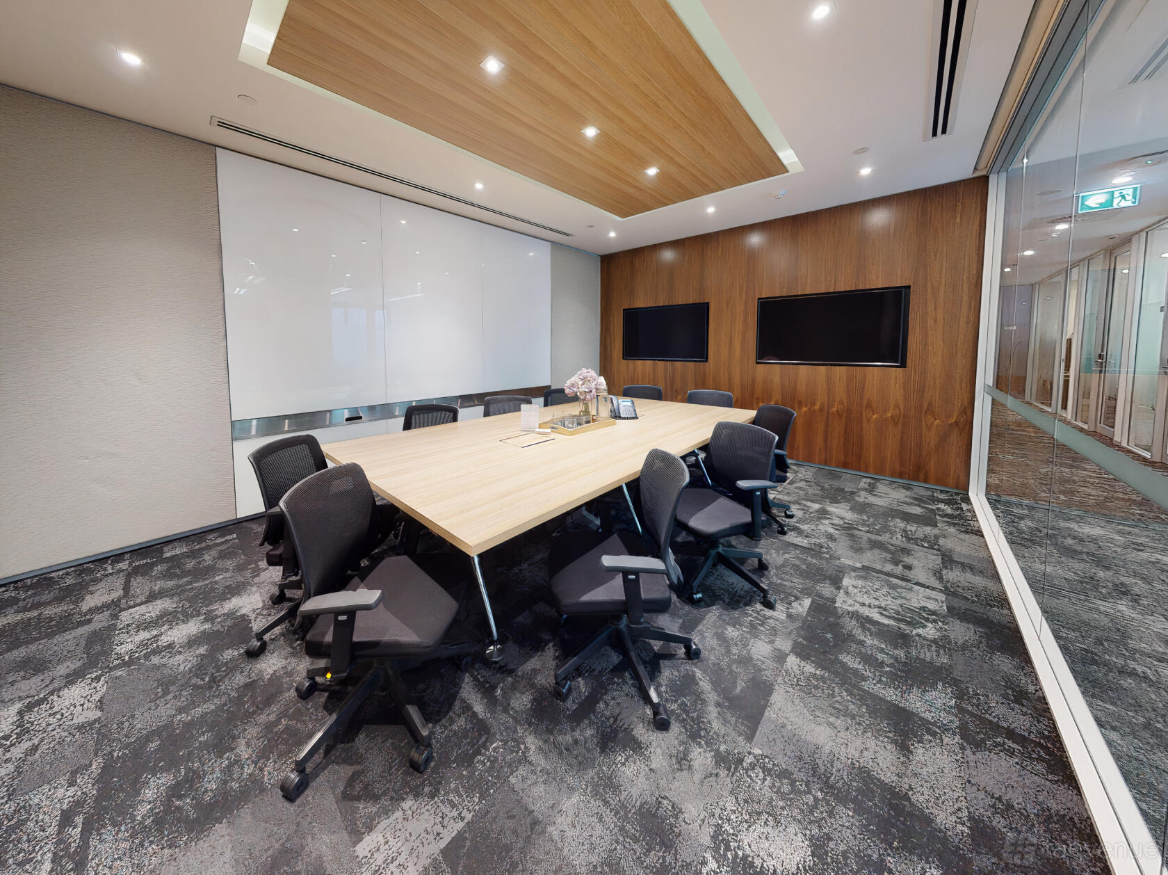 A meeting room with a hexagonal conference table, black chairs, dual wall-mounted screens, and wood paneling at Compass Offices - 9 Castlereagh Street.