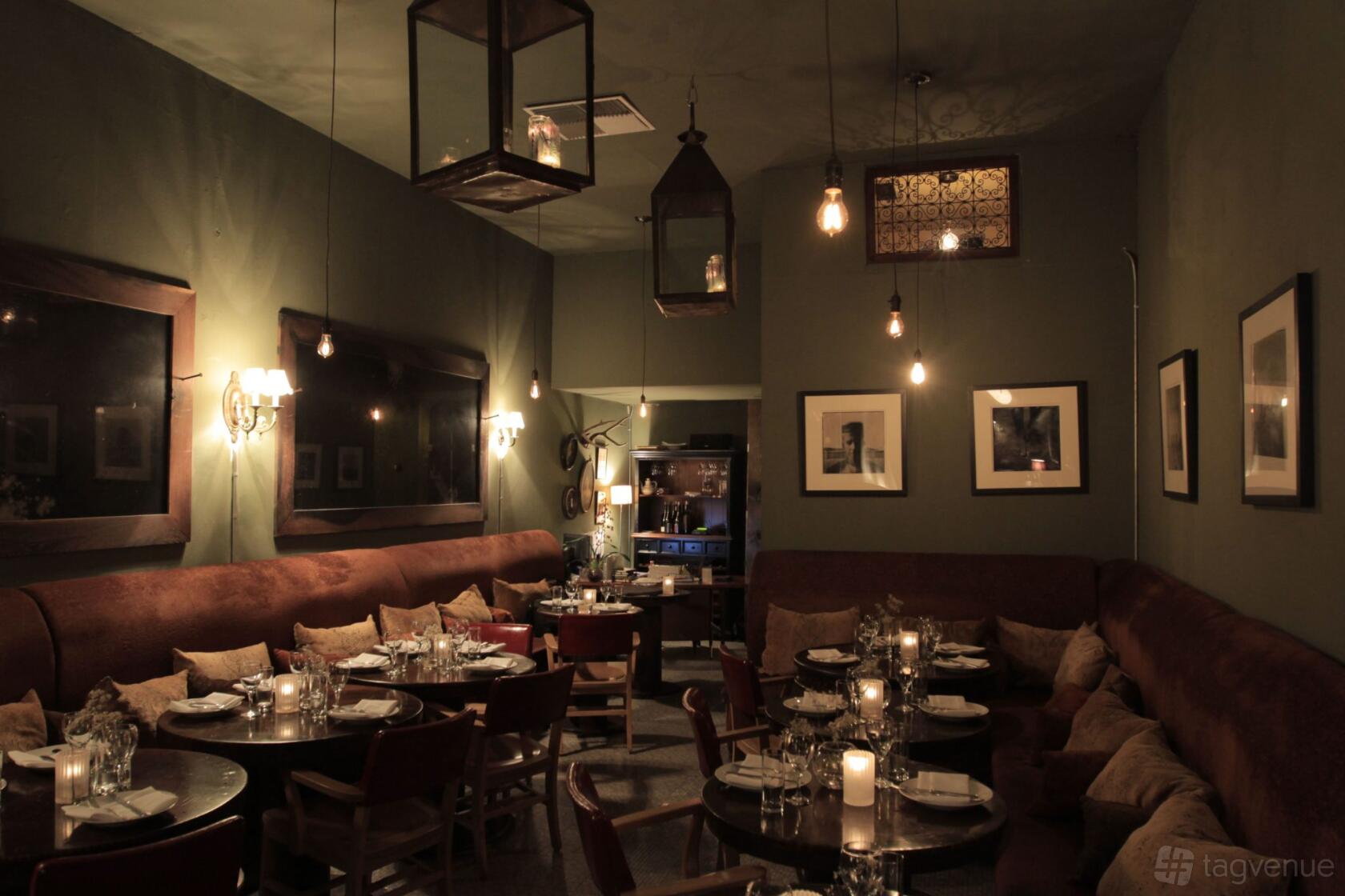 A restaurant with dim lighting, round tables set with glassware, and cushioned seating at Tagine.