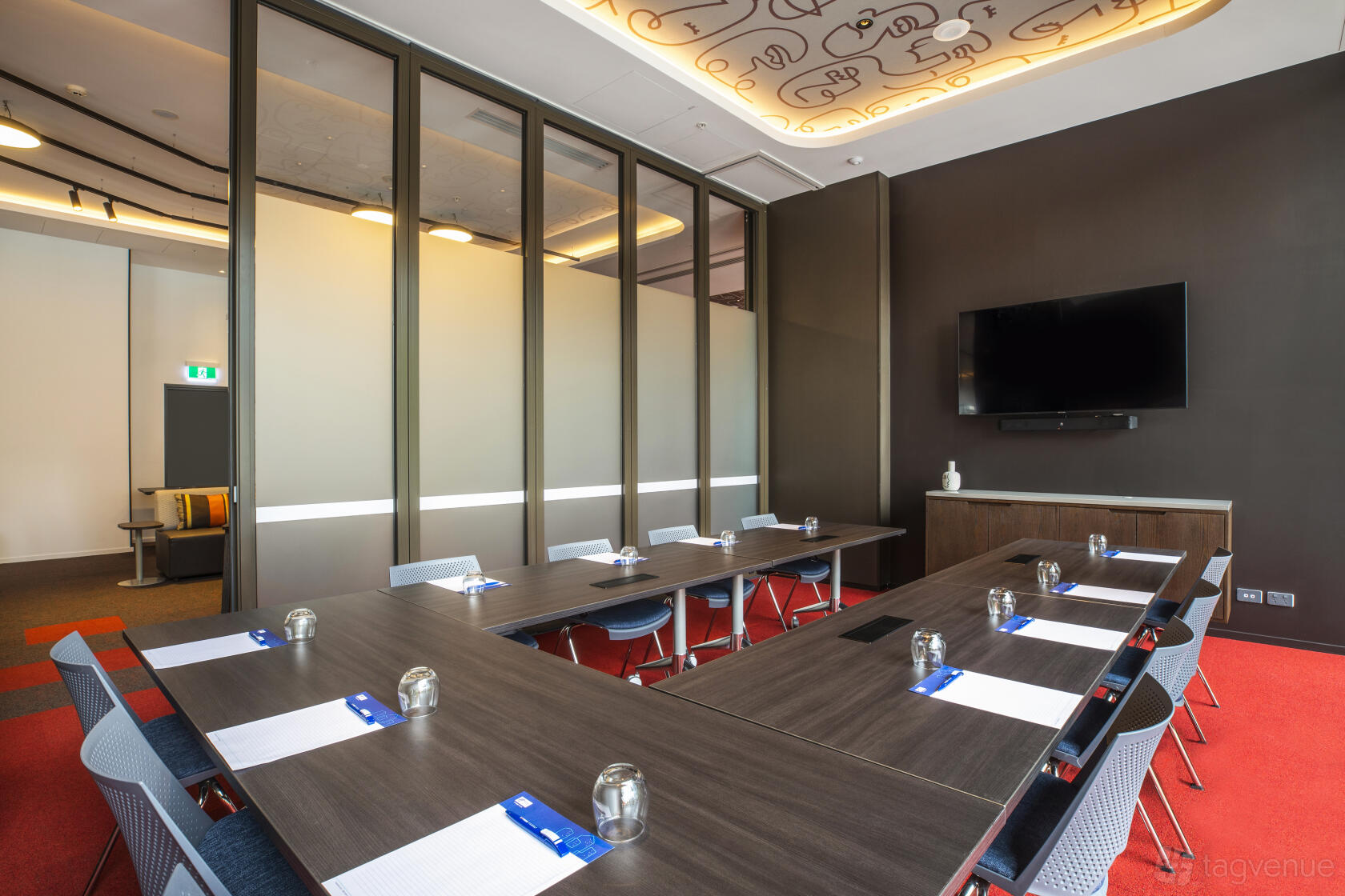 A meeting room with a U-shaped conference table, wall-mounted TV, and floor-to-ceiling glass partitions at Holiday Inn Express Little Collins.