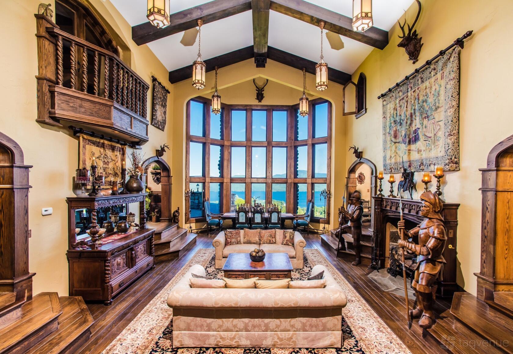 A castle interior with vaulted ceilings, large arched windows overlooking greenery, wood beams, and medieval decor at Highlands Castle.