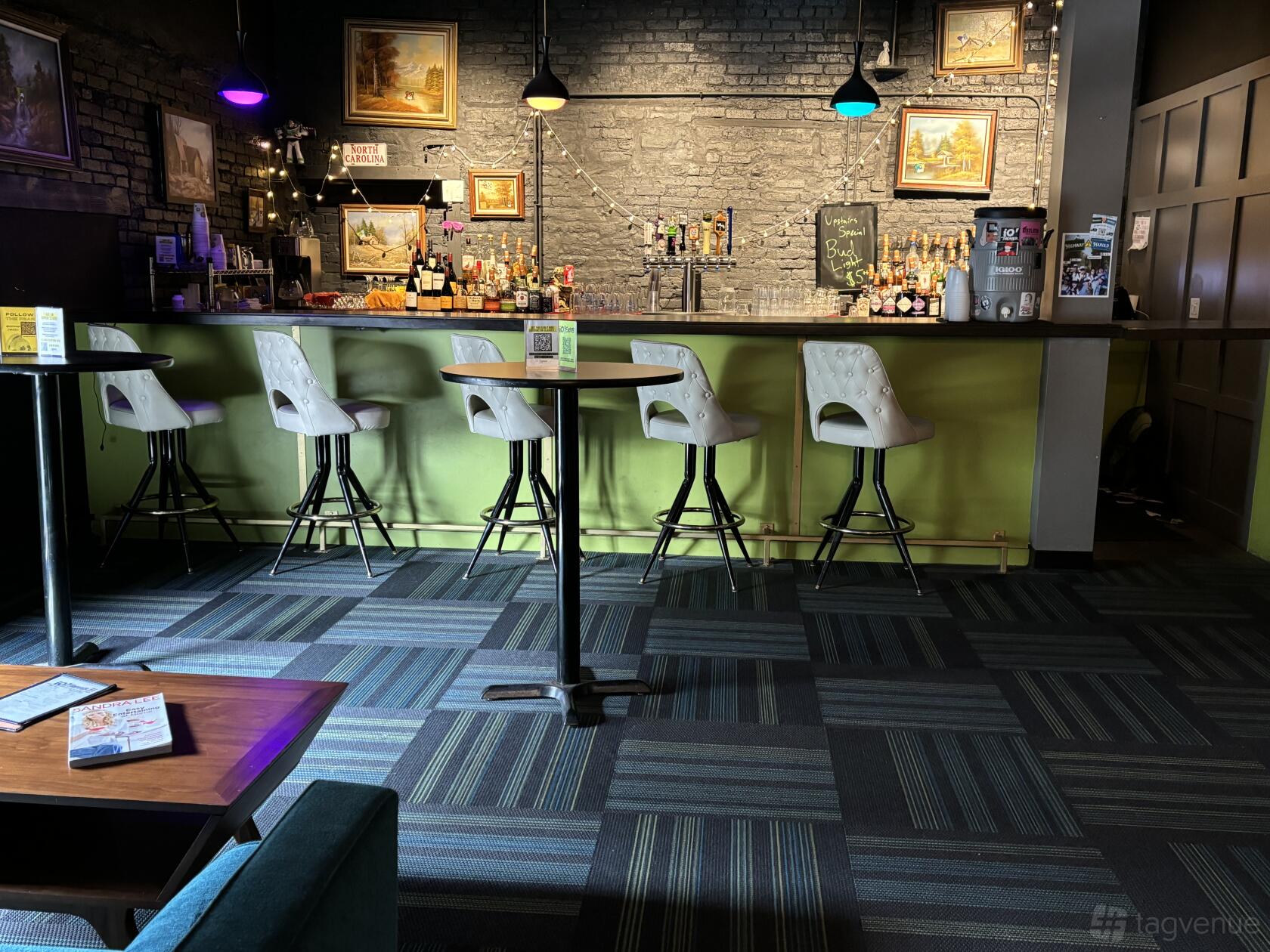 A theater event venue with a neon-lit bar, high stools, and exposed brick wall art at iO Theater.