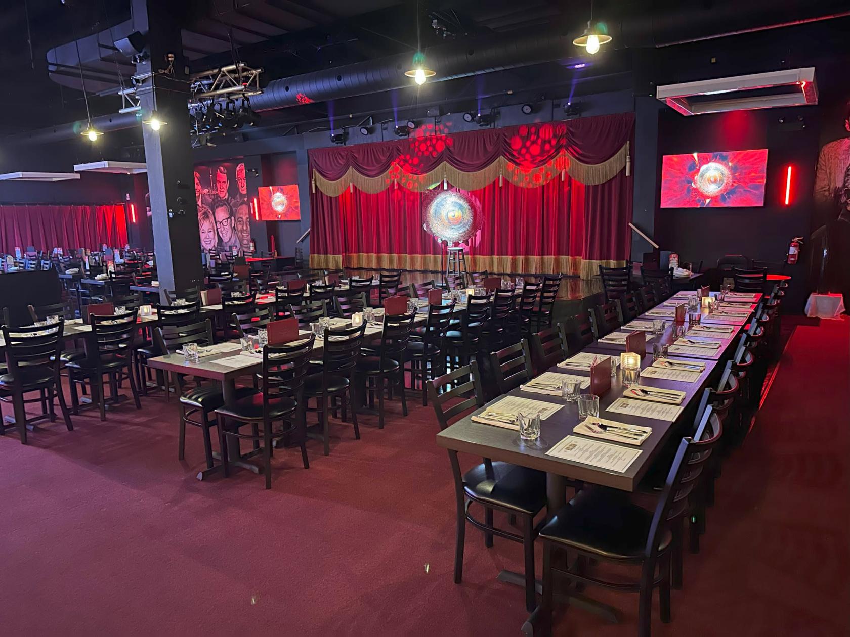 An event space with rows of black chairs and banquet tables, red drapes, and stage lighting at Jokers Theatre & Comedy Club.