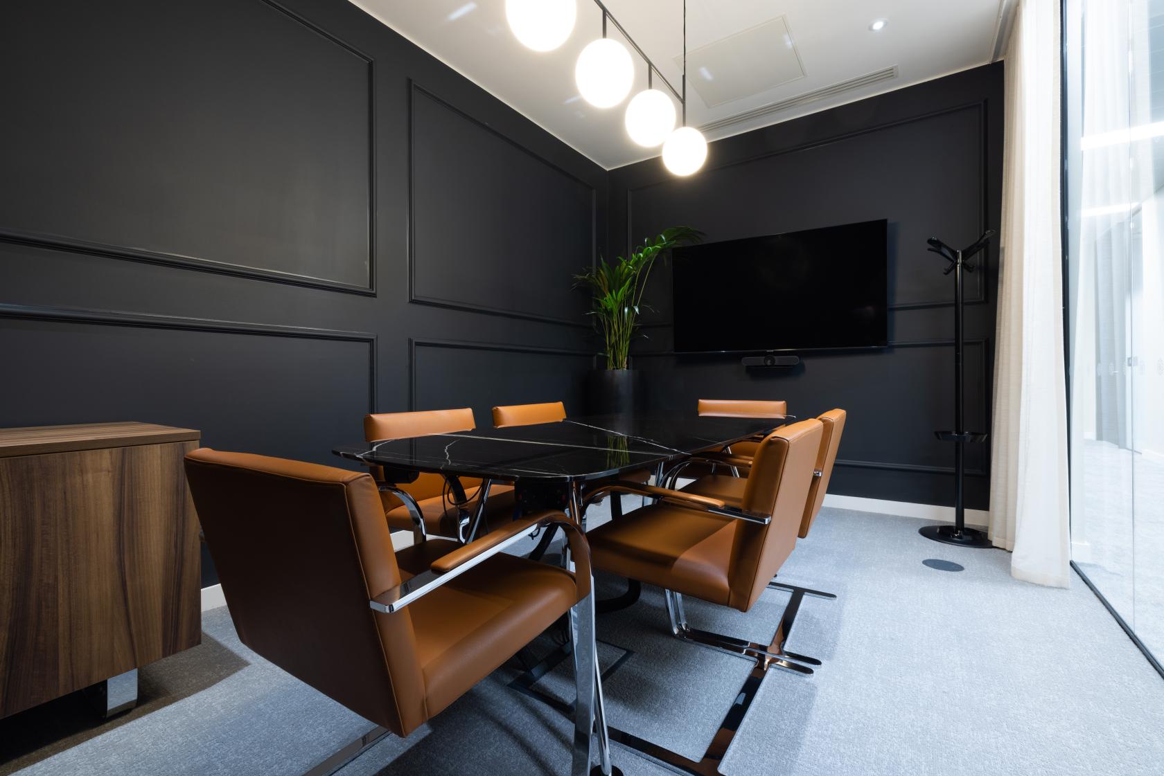A meeting room with a black accent wall, modern leather chairs, a mounted TV, and pendant lighting at Gilbanks, 11 York Street.