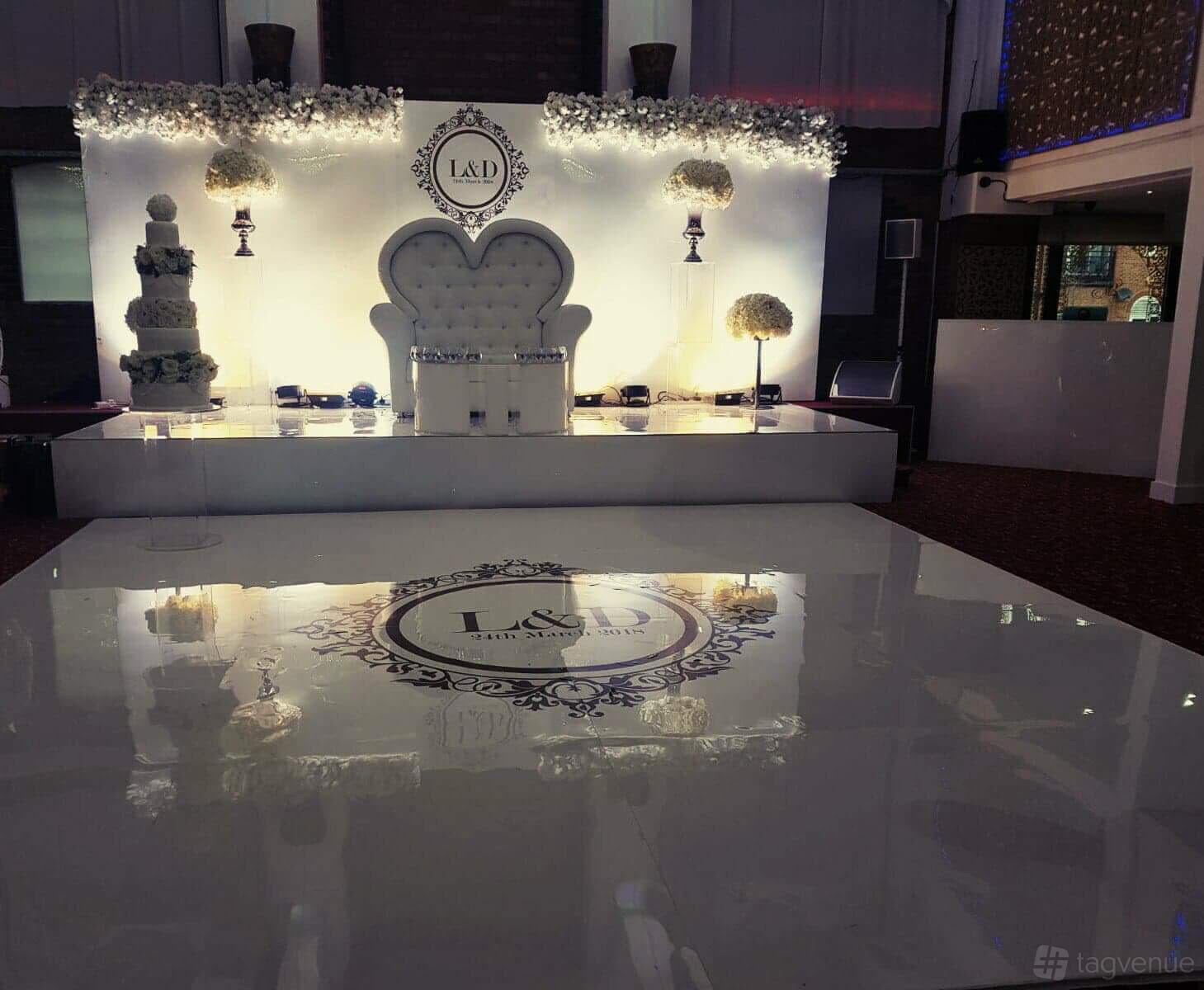 An event venue with a white stage, tufted loveseat, floral arrangements, and glossy floor at Regents Lake.
