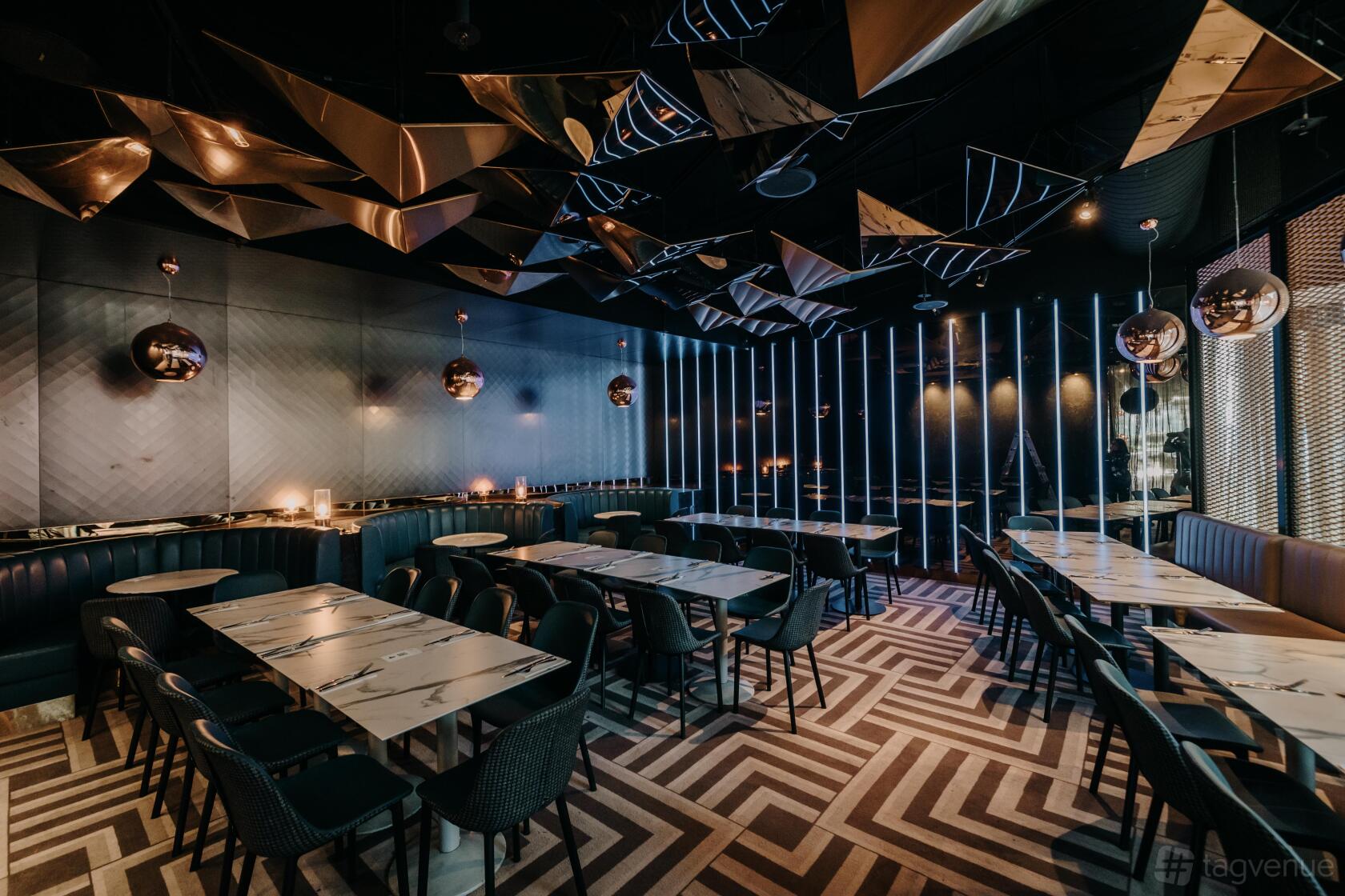 A dining room with geometric ceiling decor, patterned flooring, and marble tables at Left Bank Melbourne.