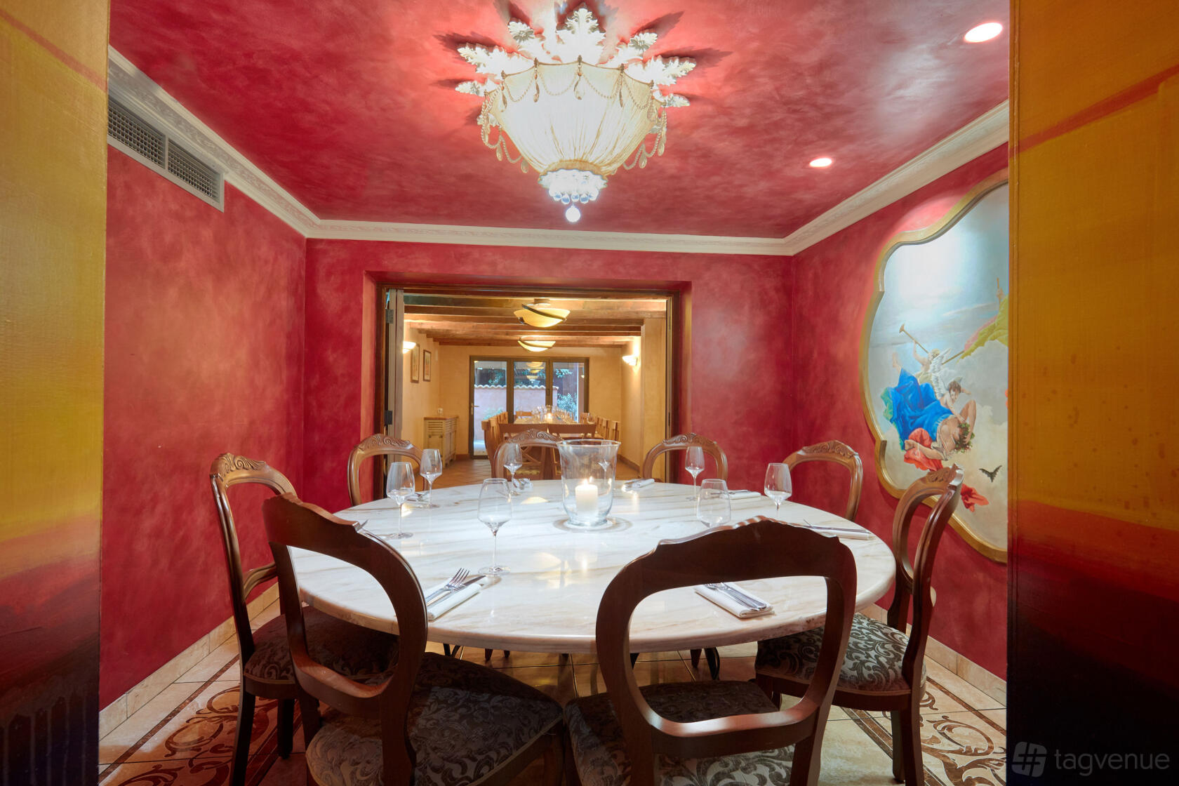 An event space in a restaurant with a round marble table, ornate chandelier, and mural accents at Stuzzichini.