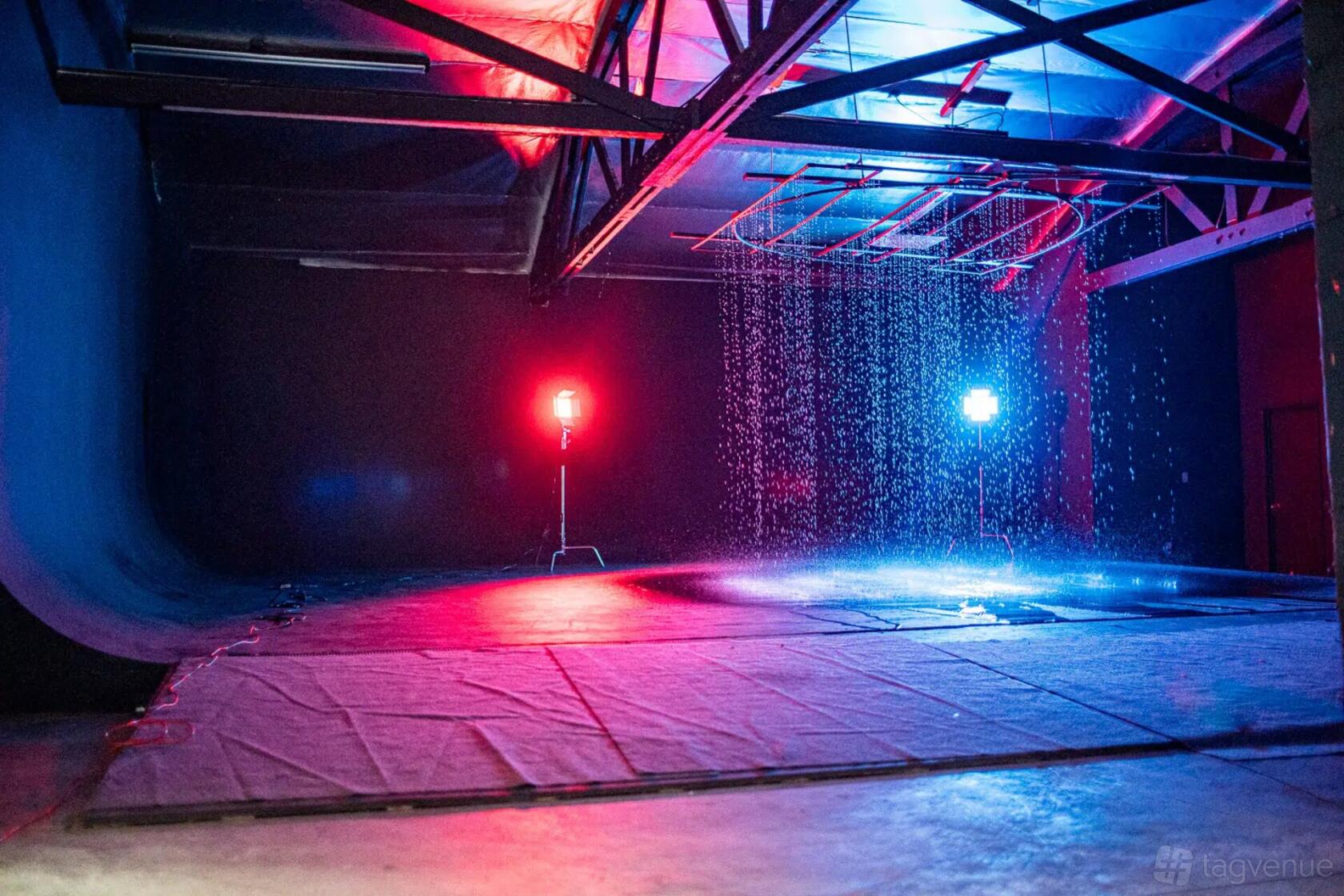 A photo studio with a black cyclorama wall, exposed ceiling beams, rainfall effect, and colored stage lights at Olympic Studios.