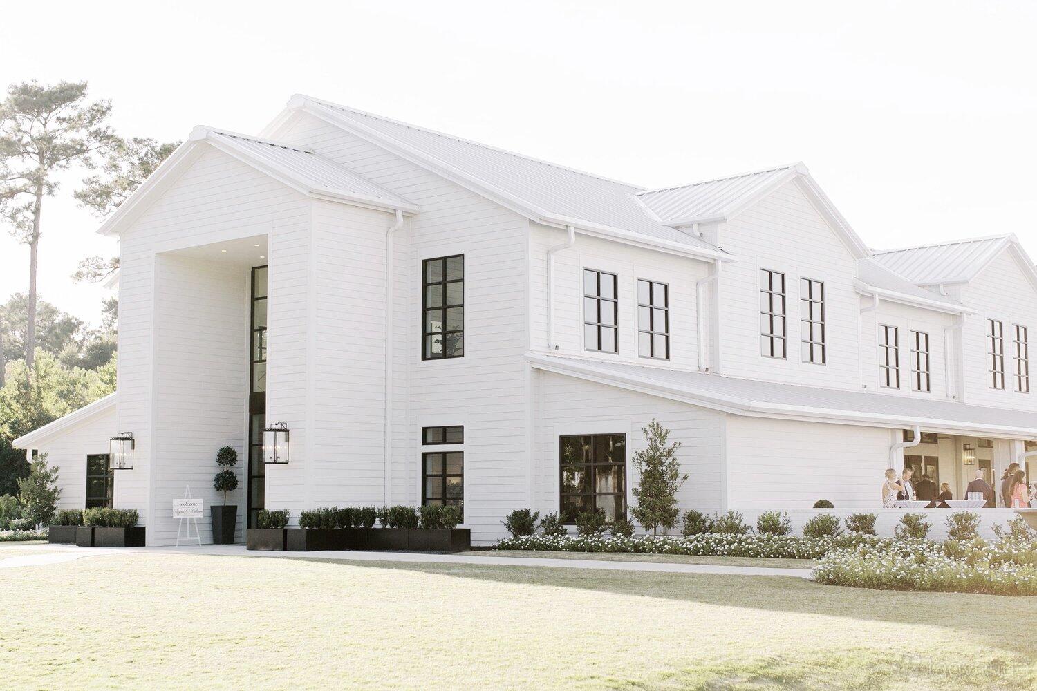 A white two-story event space with large windows, manicured landscaping, and black trim at Boxwood Manor.