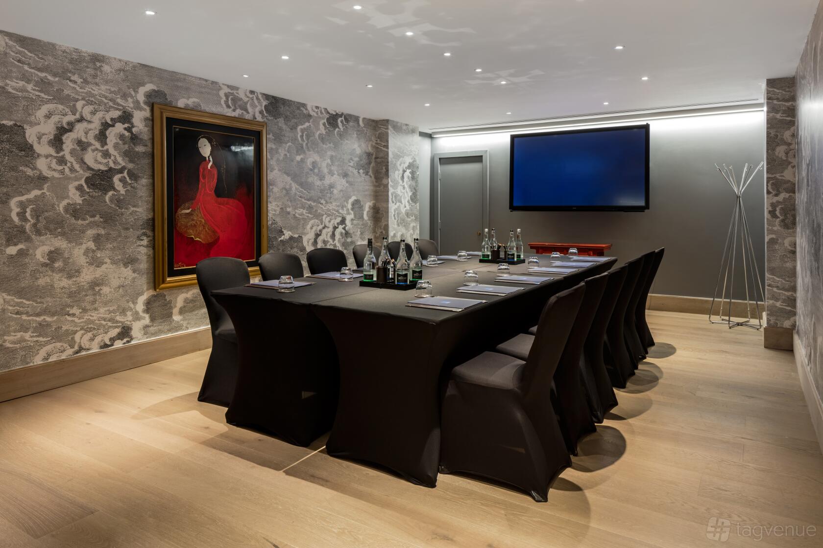 A hotel private room with a long conference table, black chairs, abstract wallpaper, and a large wall-mounted screen at Radisson Blu Hotel, London Leicester Square.