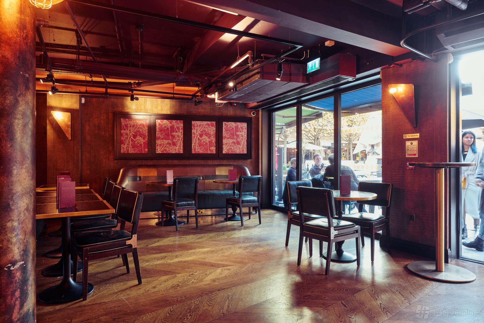 A lounge in a restaurant with wooden floors, leather chairs, and large windows at The Botanist Broadgate Circle.