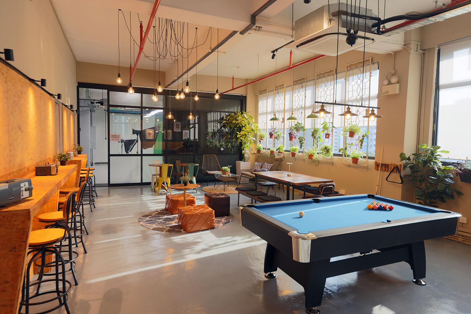 An event space with large windows, hanging Edison lights, a pool table, and plants at Alta Studio.