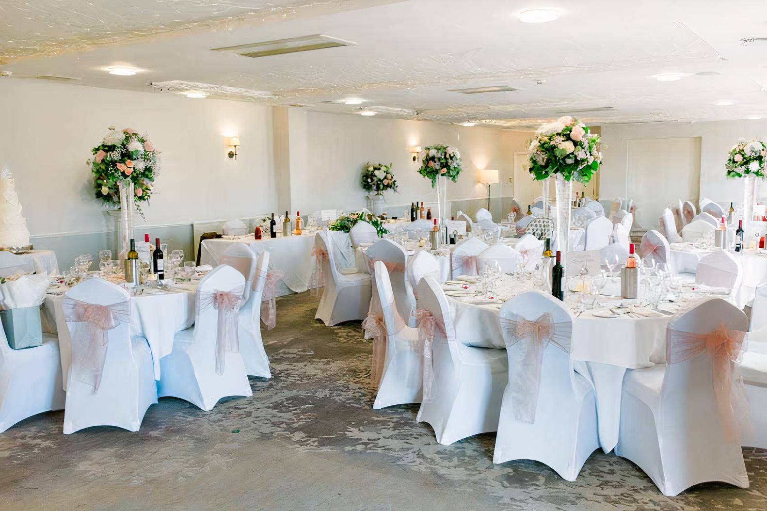 An event space with round tables dressed in white linens, floral centerpieces, and chair covers at Highfield Park.