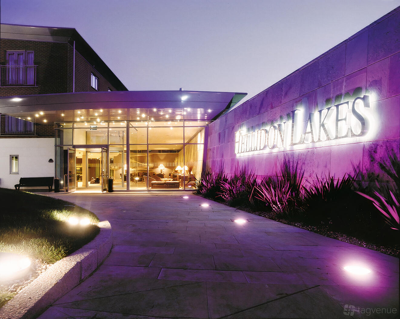 A hotel entrance with glass doors, illuminated signage, and purple accent lighting at Hellidon Lakes Golf & Spa Hotel.