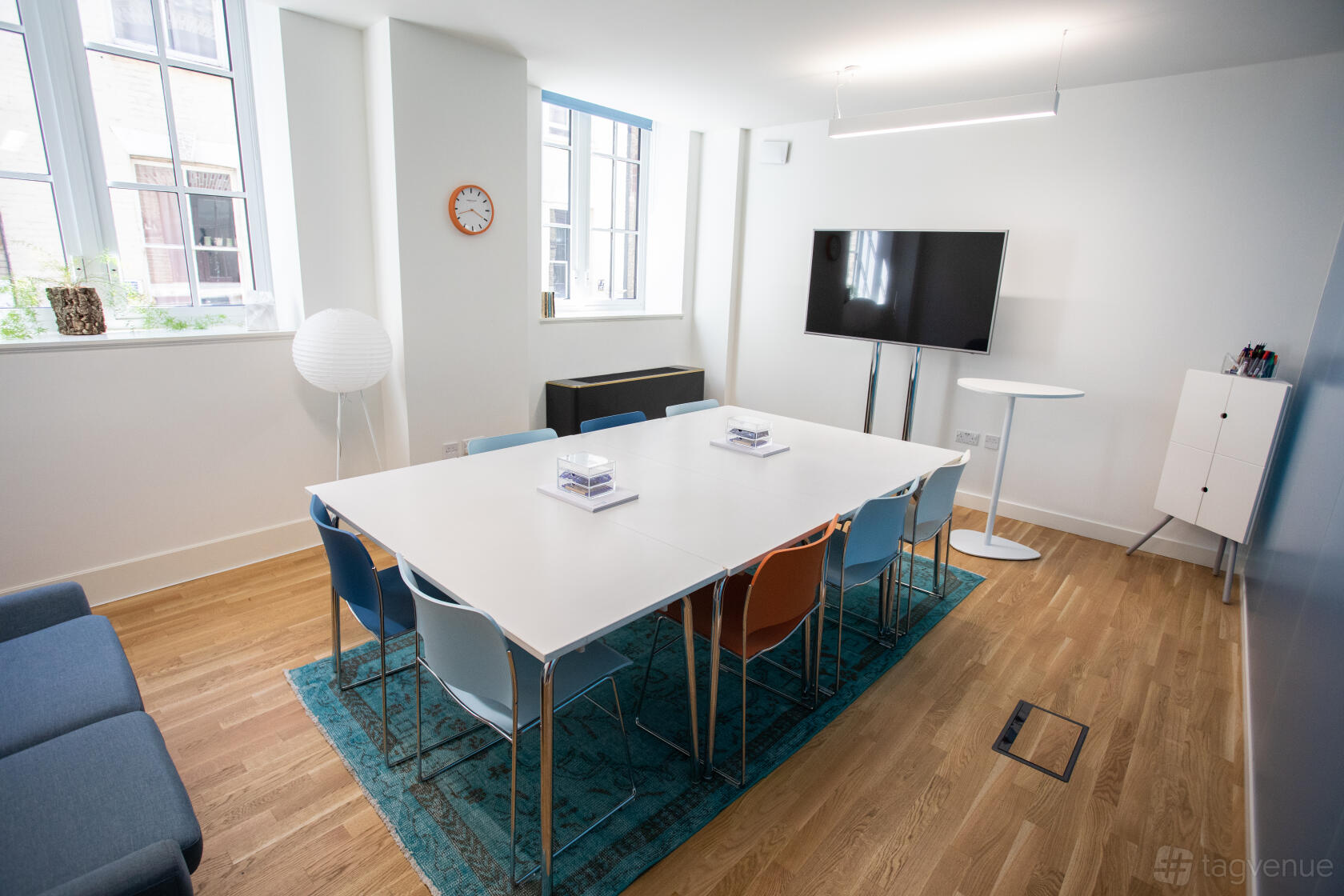 A meeting room with large windows, a rectangular table with colorful chairs, and a wall-mounted screen at Wallacespace Spitalfields.