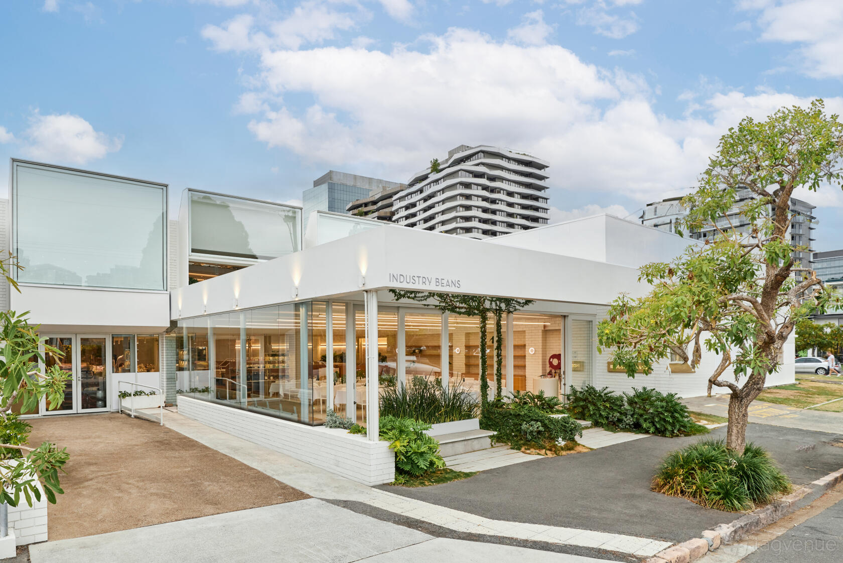 A versatile event space with a white exterior, floor-to-ceiling windows, and landscaped entrance at Industry Beans Newstead.