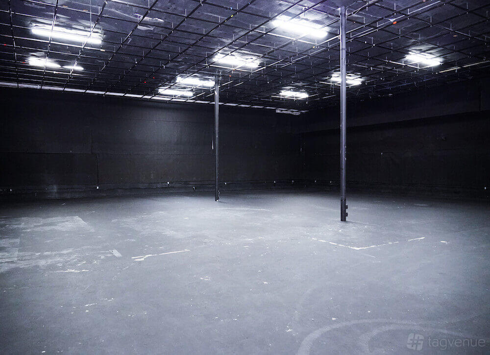 An event space with black walls, exposed ceiling grid, and overhead fluorescent lighting at M3 Studios.