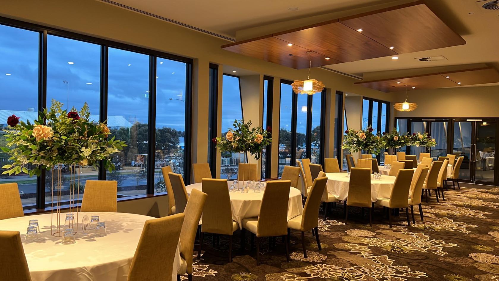 An indoor terrace room with floor-to-ceiling windows, round tables, and floral centerpieces at Highlands Hotel.