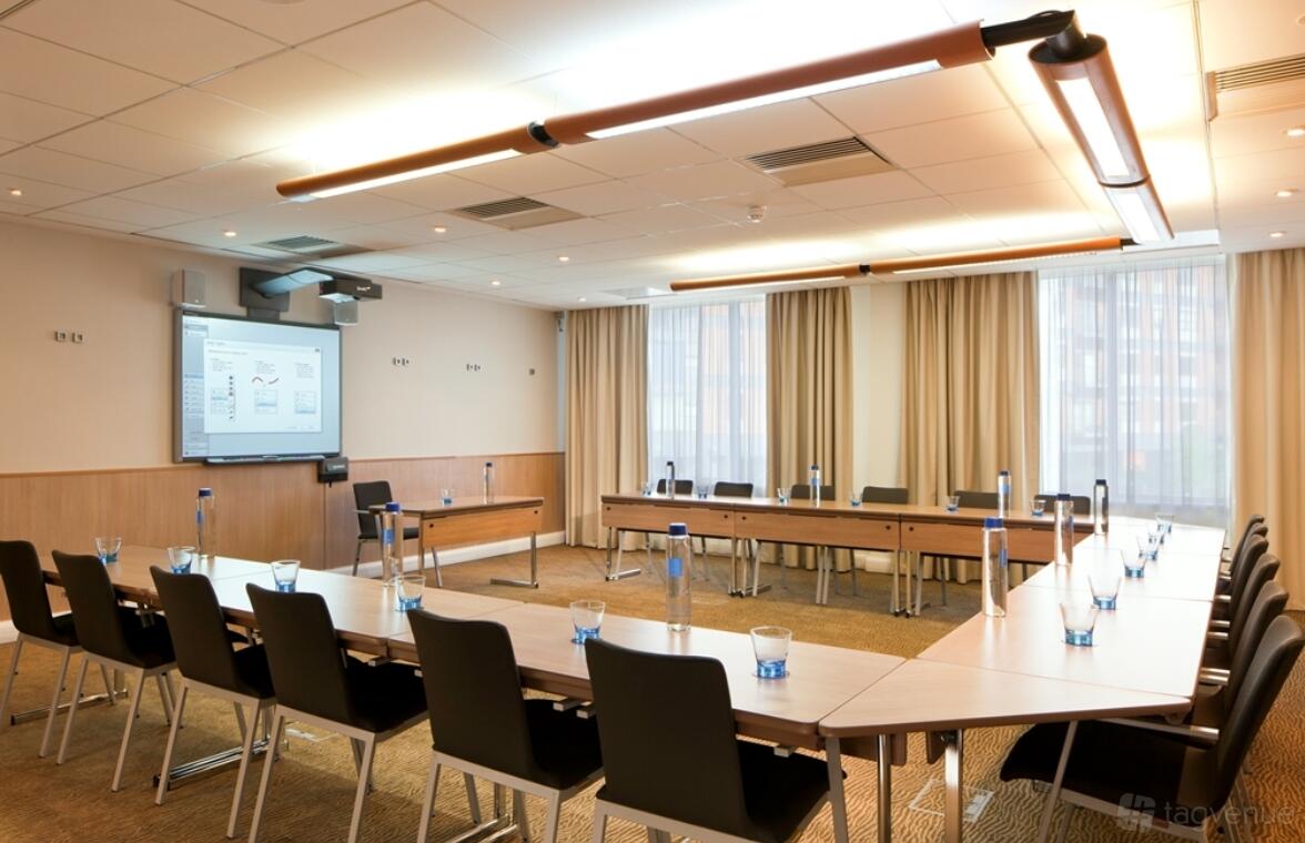 A hotel meeting room with U-shaped tables, black chairs, AV screen, and large windows at Novotel Leeds Centre.