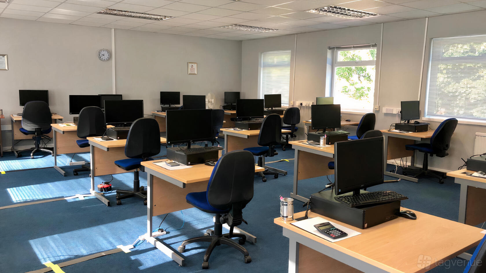 A training room with rows of desks equipped with desktop computers and blue chairs at Wesley House.