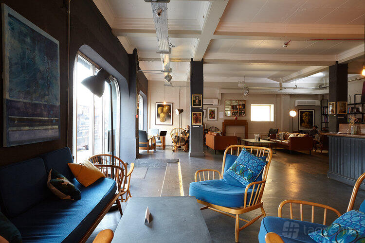 A hotel restaurant with wooden lounge chairs, cushioned seating, and artwork on dark walls at Green Rooms Hotel.