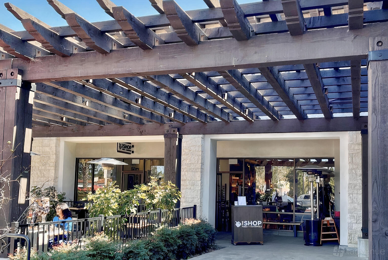 An outdoor restaurant patio with wooden pergola, open seating, and large windows at The Shop: Pizza and Cocktails.