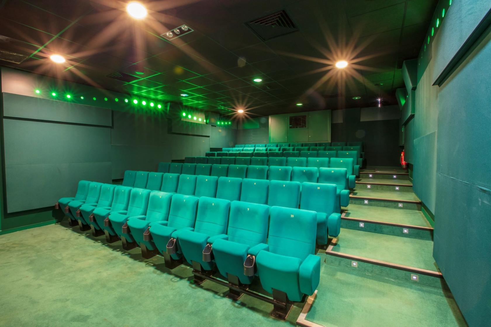 A cinema screening room with tiered rows of teal seats and green accent lighting at Curzon Wimbledon.