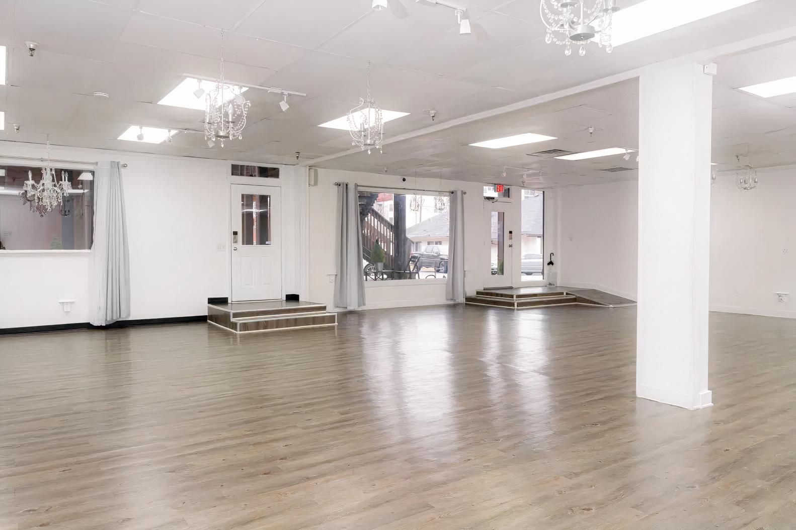 An event venue with large windows, light wood flooring, white walls, and hanging chandeliers at Space in Time.