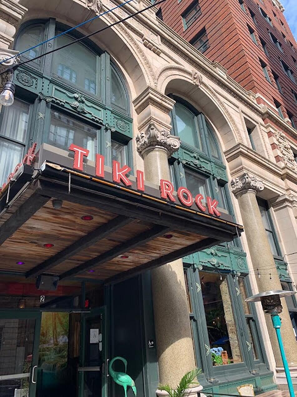 A pub with a wood-paneled entrance canopy and bold red letters above classic columns at Tiki Rock.
