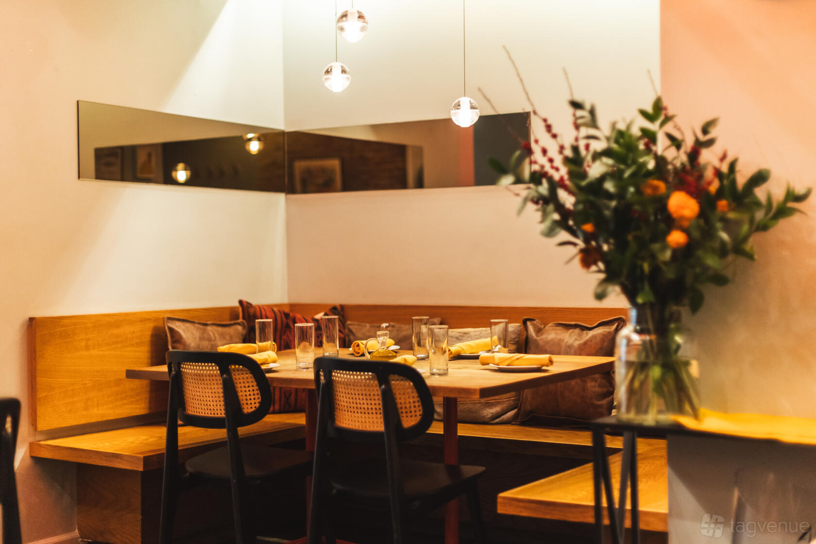 A restaurant event space with wooden booth seating, pillows, and hanging pendant lights at El Born.