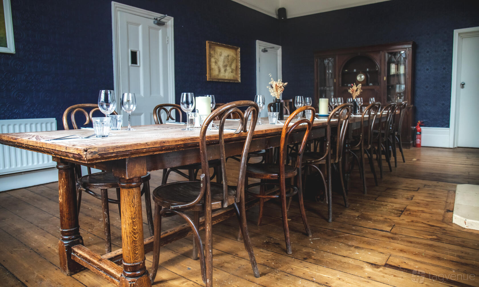 A pub dining room with a long wooden table, bentwood chairs, blue walls, and glassware at The Selkirk.