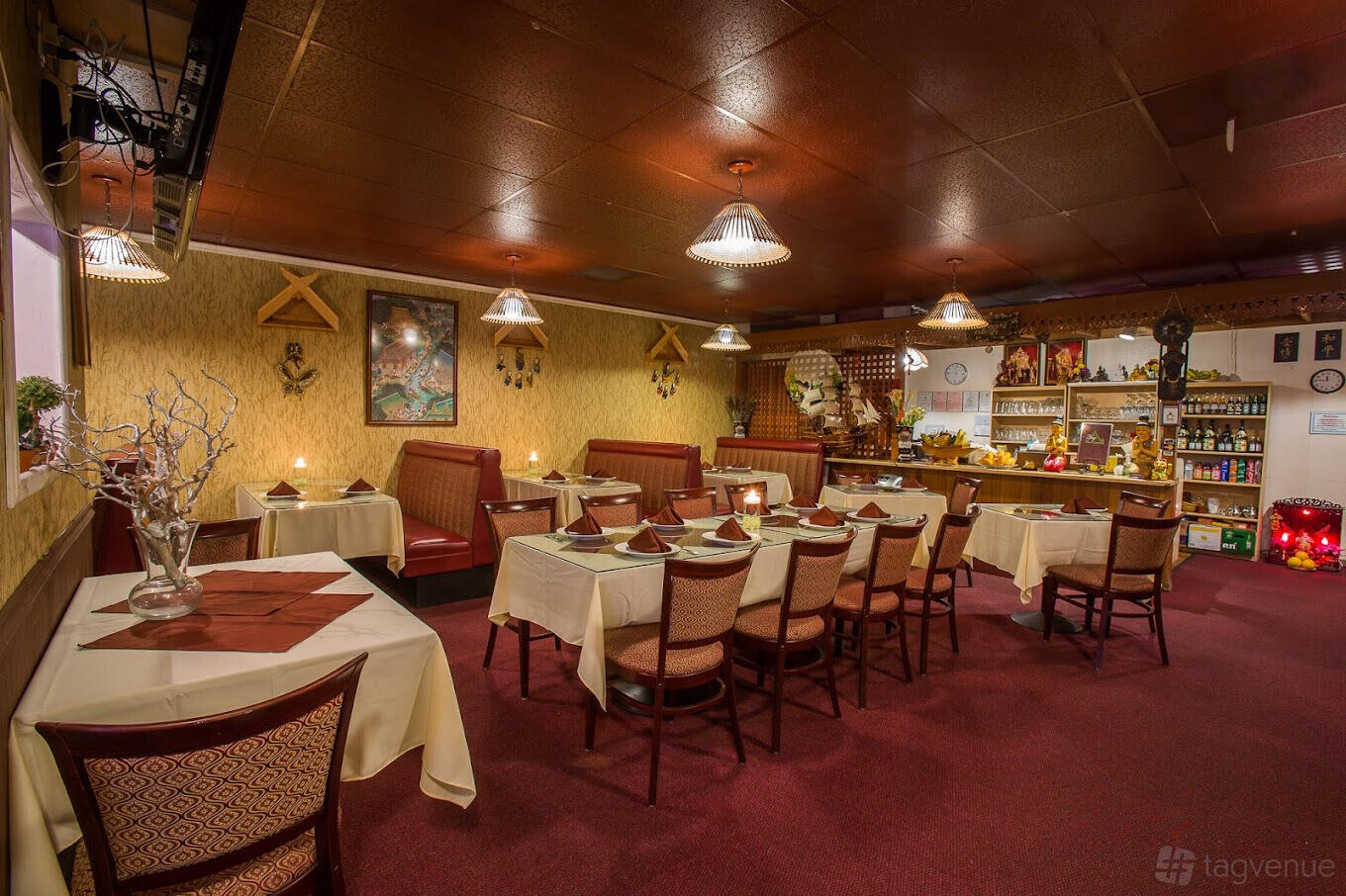 A restaurant dining room with red carpet, booth seating, square tables with folded napkins, and warm pendant lighting at Top Thai Cuisine.