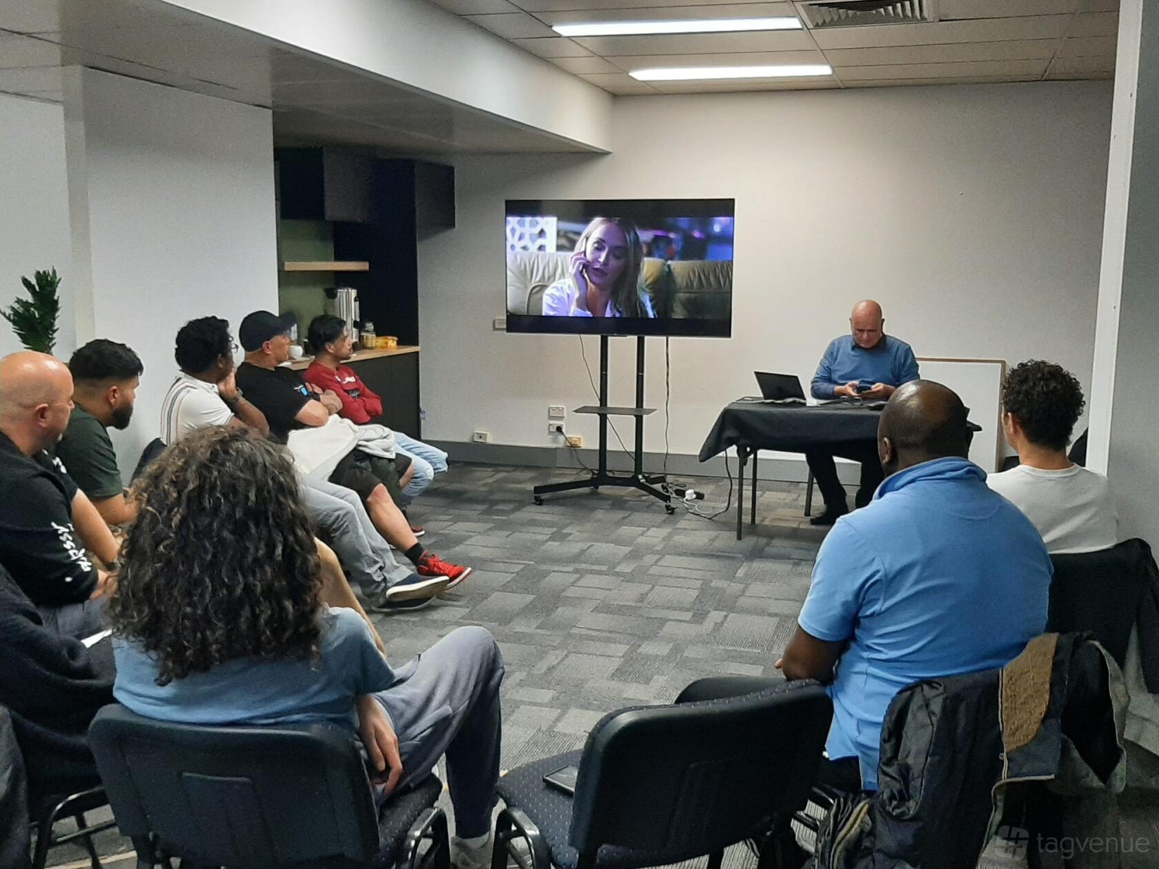 A warehouse meeting room with carpeted floors, overhead lighting, and a large screen at Australian Film Central.