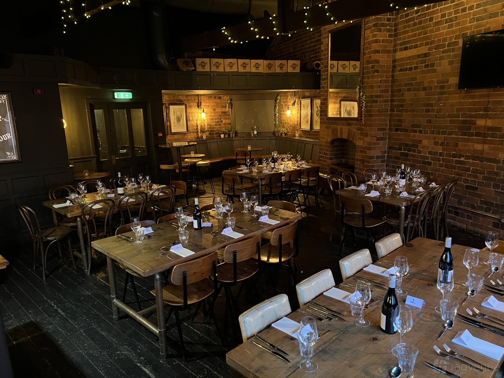 A function room with exposed brick walls, wooden tables set with glassware and wine bottles at The Distillery.
